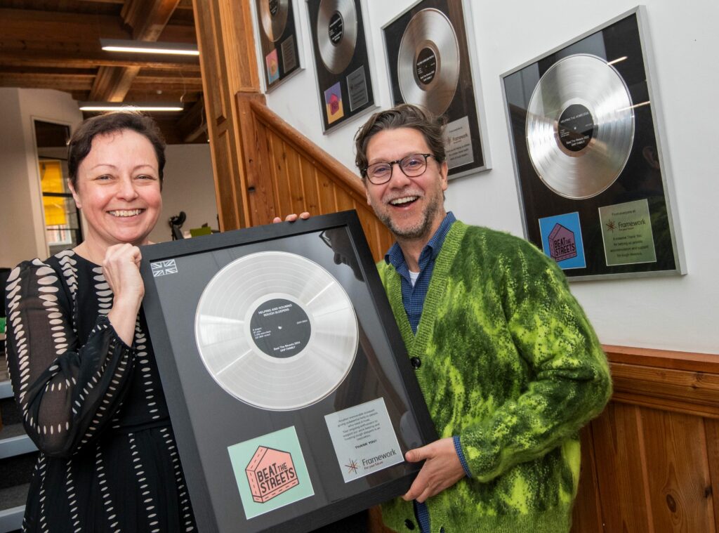 Claire McGonigle and George Akins holding the Beat the Streets 2024 gold disk presented in recognition of their fundraising for Framework.