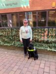 Framework volunteer Kay standing outside the Wellbeing Hub in Nottingham with her Guide Dog. She is smiling at the camera.