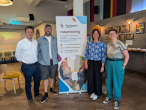 Framework staff at Sobar in Nottingham during Volunteers' Week standing with a Framework branded banner with volunteering information on it. There are four members of staff smiling