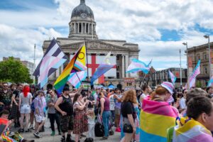 A crowd photo at Nottingham Pride 2025 with flags waving in the air against blue cloudy but sunny sky,